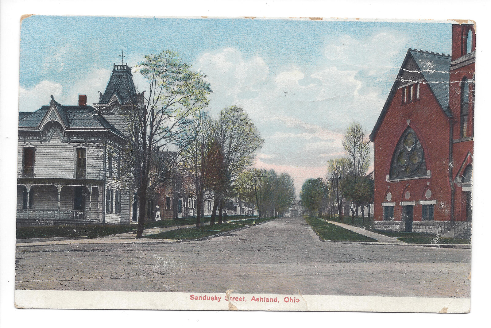 Color postcard captioned Sandusky Street, Ashland, Ohio, showing an ornate house at left and a red brick church at right.